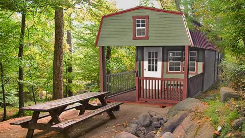 Green hunting cabin in a forested area with a picnic table out front