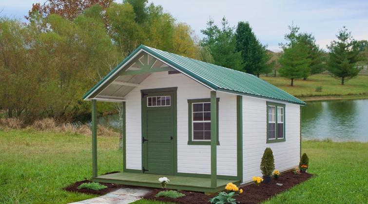 Signature Hunter Cabin with white LP Barn Siding, green trim, a green front porch, green front door, and green roof in front of a creek.